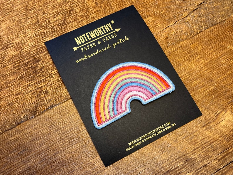 Pu&ograve; includere: Un cerotto ricamato a forma di arcobaleno su una carta nera con il testo "NOTEWORTHY PAPER & PRESS embroidered patch" e "WWW.NOTEWORTHYSTORE.COM original design &copy; noteworthy paper & press, llc".