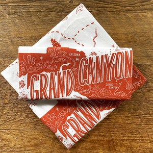 May include: Two white tea towels with a red print of a map of the Grand Canyon. The map includes the Colorado River and the text "Grand Canyon".