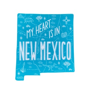 May include: A blue sticker with a white outline of the state of New Mexico. The sticker has a white graphic design with the text "My heart is in New Mexico".