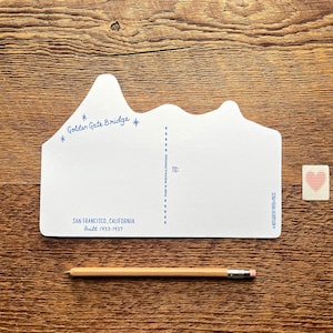 May include: A white postcard shaped like the Golden Gate Bridge with the text "Golden Gate Bridge" and "San Francisco, California Built 1933-1937". The postcard has a blank space for writing a message and a space for the recipient's address.