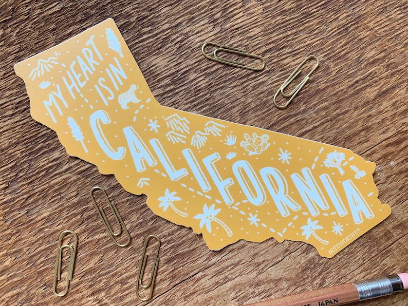 May include: Yellow sticker shaped like the state of California with the text "My heart is in California" and various illustrations of mountains, palm trees, cacti, and stars.
