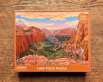 May include: A 1,000 piece jigsaw puzzle featuring a scenic view of Zion National Park in Utah. The puzzle box shows a colorful illustration of the park's iconic red rock cliffs, with a winding road leading through the canyon. Two bighorn sheep are in the foreground, looking out over the landscape. The box also includes the text "Zion National Park" and "1,000 Piece Puzzle".