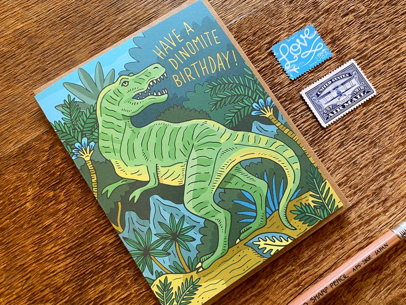 Op de afbeelding: Een groene dinosaurus met gele strepen staat in een jungle-omgeving. De kaart luidt "Have a Dinomite Birthday!"