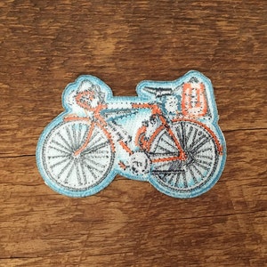 May include: A blue and orange embroidered patch of a bicycle with a small bag on the back.