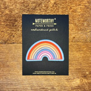 Pu&ograve; includere: Un cerotto ricamato a forma di arcobaleno su sfondo nero. Il cerotto &egrave; di Noteworthy Paper & Press e dice "embroidered patch" in lettere dorate.
