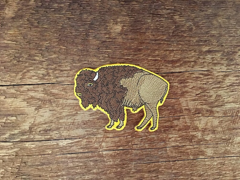 K&ouml;nnte beinhalten: Ein braunes gesticktes Patch mit einem Bison mit gelber Umrandung. Der Bison blickt nach links und hat ein wei&szlig;es Horn.
