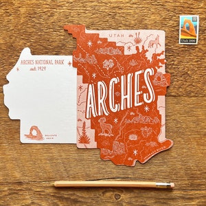 May include: A postcard featuring a map of Arches National Park in Utah. The postcard is shaped like the park and features a red and pink color scheme. The text "Arches" is written in large white letters across the map. The postcard also includes the text "Utah 1988" in the upper right corner.