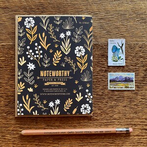 May include: A black and gold floral patterned notebook with the text "NOTEWORTHY Paper & Press Missoula, Montana Est. 2008" and the website address "www.noteworthystore.com".