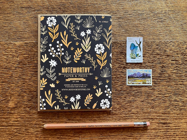 May include: A black and gold floral patterned notebook with the text "NOTEWORTHY Paper & Press Missoula, Montana Est. 2008" and the website address "www.noteworthystore.com".