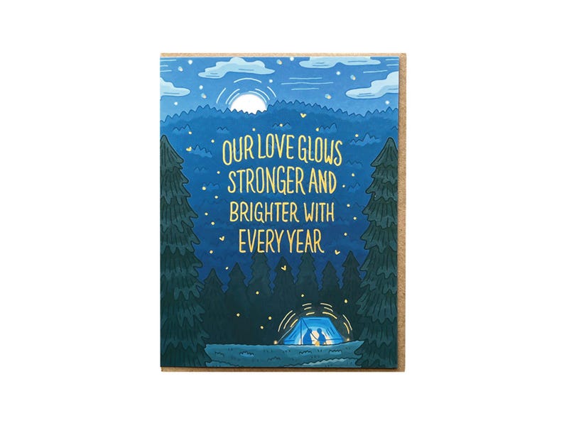 May include: An illustrated card in blue and green colours featuring a couple camping in a tent under a starry night sky. The text reads "Our love glows stronger and brighter with every year."