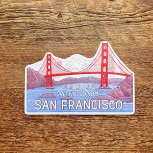 May include: A sticker featuring a red and white illustration of the Golden Gate Bridge in San Francisco, California. The sticker has a blue background with the text "Greetings from San Francisco" at the bottom.
