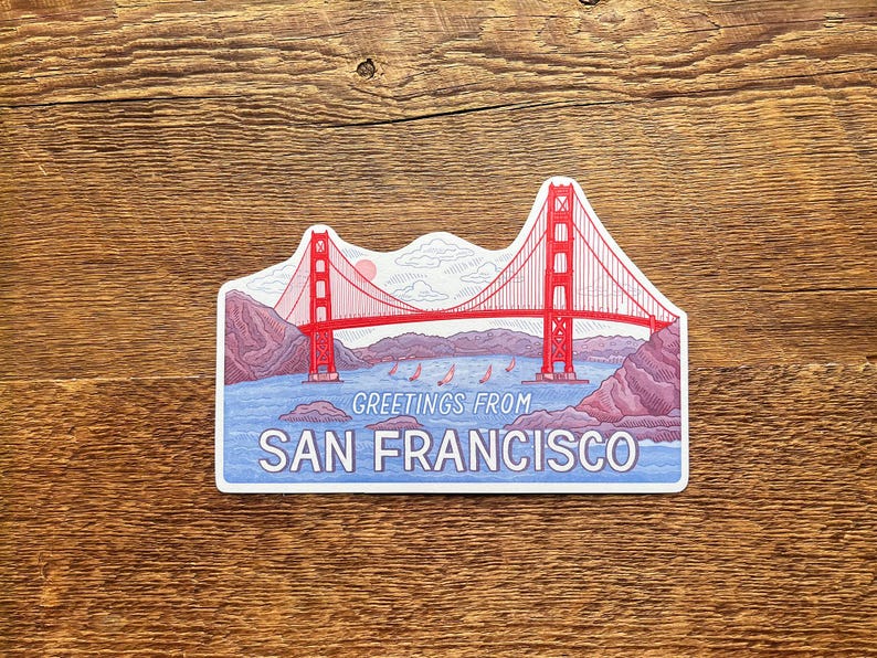 May include: A sticker featuring a red and white illustration of the Golden Gate Bridge in San Francisco, California. The sticker has a blue background with the text "Greetings from San Francisco" at the bottom.