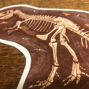 Peut inclure: Illustration d'un squelette de dinosaure fossile brun et blanc sur fond blanc. Le dinosaure est couch&eacute; sur le c&ocirc;t&eacute;, la t&ecirc;te tourn&eacute;e vers la gauche. L'illustration est d&eacute;taill&eacute;e et r&eacute;aliste.