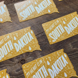 Pu&ograve; includere: Pi&ugrave; adesivi gialli con il contorno dello stato del Dakota del Sud e il testo "My heart is in South Dakota".