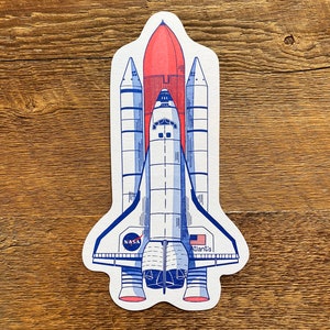 May include: A white and blue space shuttle with a red rocket booster, labeled "NASA" and "Atlantis".