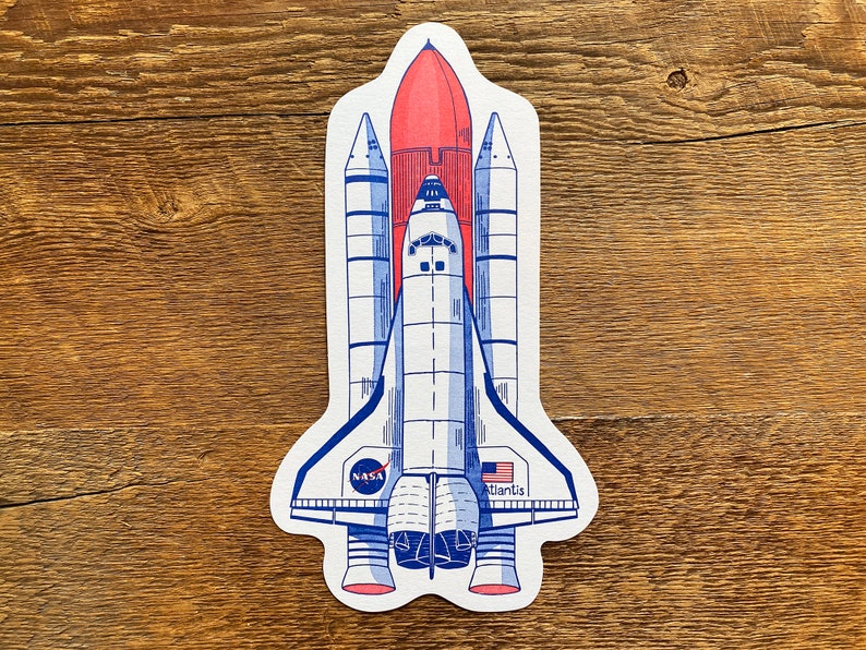 May include: A white and blue space shuttle with a red rocket booster, labeled "NASA" and "Atlantis".