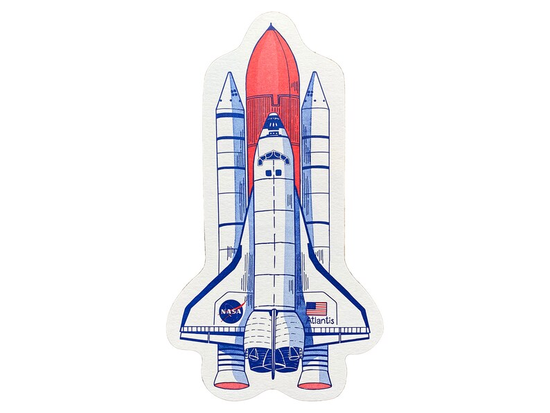 May include: A white and blue space shuttle with a red rocket booster. The shuttle is labeled "NASA" and "Atlantis".