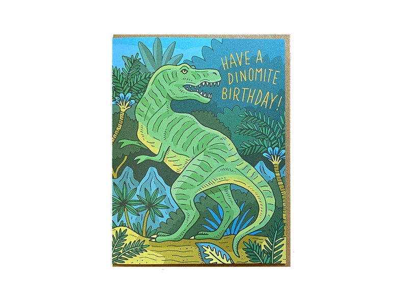 Op de afbeelding: Een groene dinosaurus met een tandenrij staat in een jungle-omgeving met palmbomen en blauwe bloemen. De tekst "Have a Dinomite Birthday!" is geschreven in gouden letters.