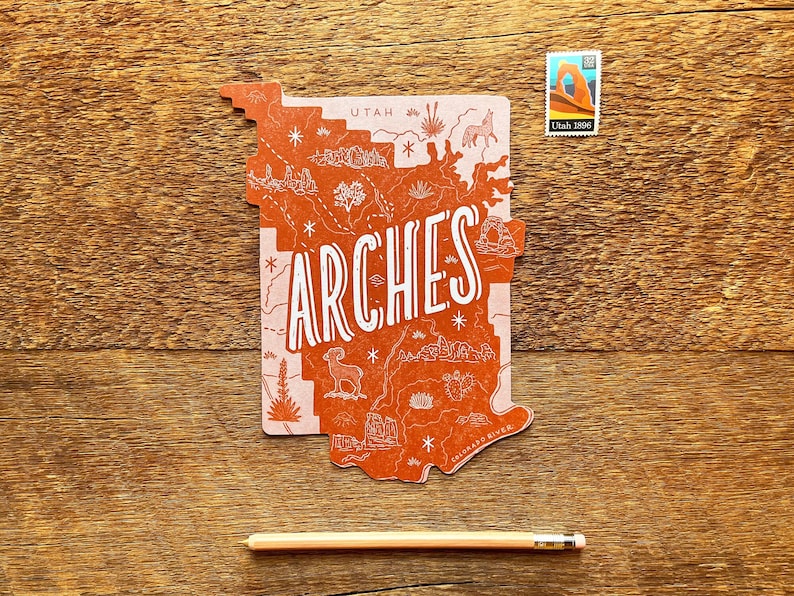 May include: A red and pink illustrated map of Arches National Park in Utah. The map features a white outline of the park with various landmarks and details. The word "ARCHES" is written in large white letters across the center of the map.