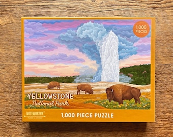 May include: A 1,000 piece jigsaw puzzle featuring a scenic view of Yellowstone National Park. The puzzle depicts a geyser erupting with a cloudy sky and three bison in the foreground. The puzzle box is orange with the text "Yellowstone National Park" and "1,000 Piece Puzzle".