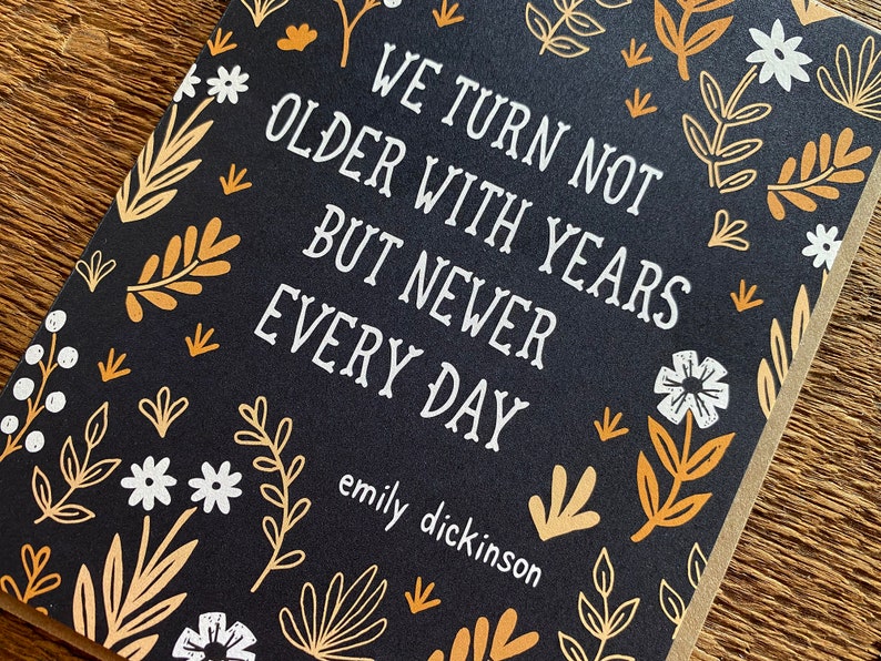 May include: A black card with a white floral pattern and the text "We turn not older with years but newer every day" by Emily Dickinson.