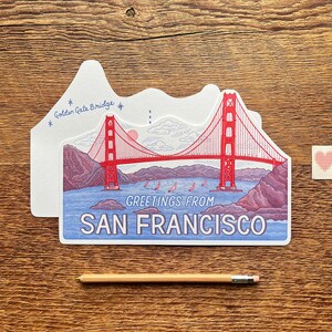 May include: A postcard featuring a red and white illustration of the Golden Gate Bridge in San Francisco, California. The postcard says "Greetings from San Francisco" and "Golden Gate Bridge".