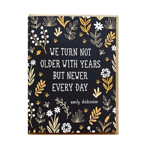 May include: A black card with a floral pattern in gold and white. The card has the text "We turn not older with years but newer every day" and "emily dickinson" at the bottom.