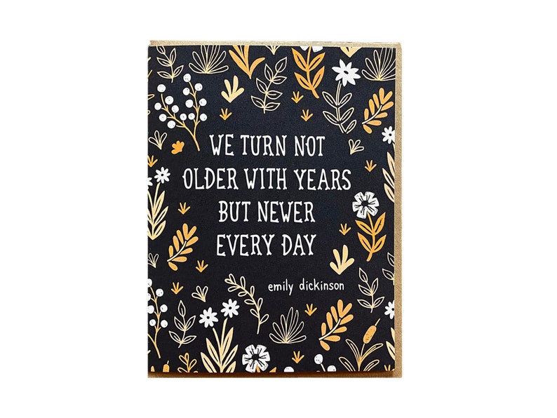 May include: A black card with a floral pattern in gold and white. The card has the text "We turn not older with years but newer every day" and "emily dickinson" at the bottom.