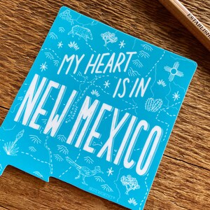 May include: A blue sticker with a white outline of the state of New Mexico. The sticker says "My heart is in New Mexico" with a stylized map of the state in the background.