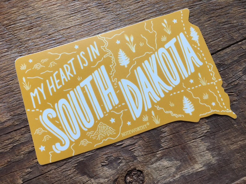 Pu&ograve; includere: Adesivo giallo con un contorno bianco dello stato del Dakota del Sud. L'adesivo dice "My heart is in South Dakota" e ha un piccolo logo "Noteworthy" in basso a destra.