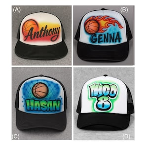 May include: Four black and white trucker hats with basketball-themed designs. Each hat features a basketball and a name: Anthony, Genna, Hasan, and Nico. The hats have a white front panel and a black brim and mesh back.