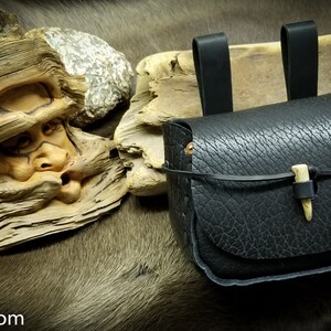 May include: A black leather pouch with a bone toggle closure. The pouch has two leather straps for hanging.