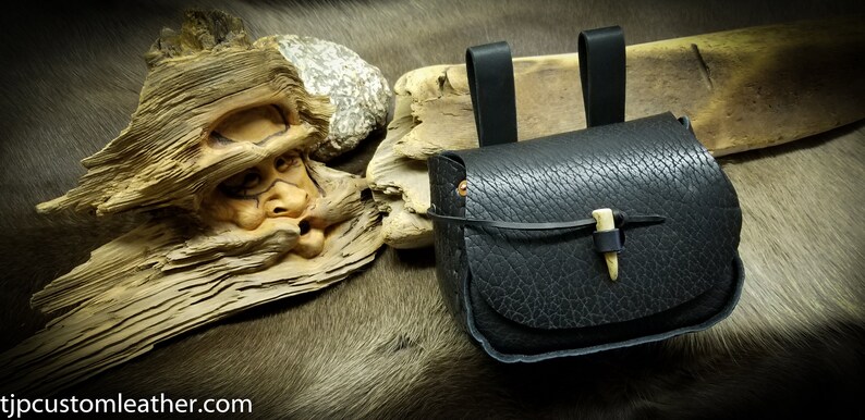 May include: A black leather pouch with a bone toggle closure. The pouch has two leather straps for hanging.