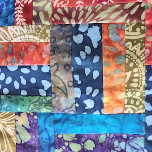 May include: Close-up of a colorful patchwork quilt with a variety of patterned fabric strips. The quilt features a mix of blues, oranges, greens, and purples, with intricate designs and textures. The quilt is a handmade textile.