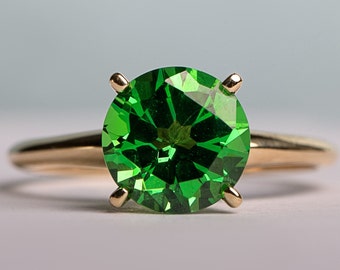 May include: A gold ring set with a large, round, emerald green gemstone.