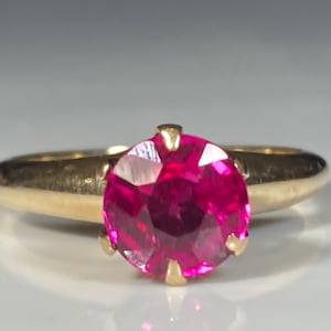 May include: A gold ring set with a large, round, faceted ruby gemstone.