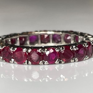 May include: A silver band ring set with a row of red ruby gemstones.