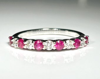 May include: A silver ring featuring a row of alternating round-cut rubies and diamonds. The gemstones are set closely together, creating a continuous band of color and sparkle. The ring is displayed on a white surface.