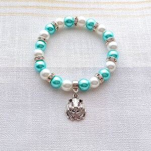 May include: A white and turquoise beaded bracelet with a silver charm of a guinea pig. The bracelet has small clear rhinestones on each bead.