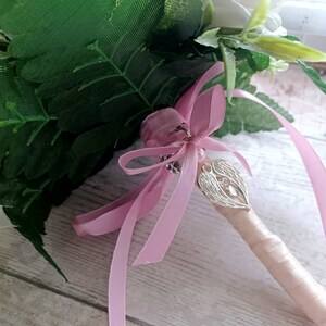 May include: A pink satin ribbon tied around a bouquet of white flowers with a silver angel wing charm attached.
