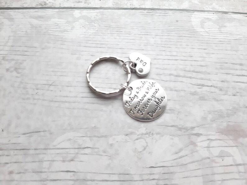 May include: Silver keychain with a round charm that reads "Today a Bride, Tomorrow a Wife, Forever your Daughter". A small heart charm with the word "Dad" is attached to the keychain.