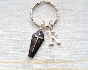 May include: A silver key chain with a black coffin charm and a silver charm with the letter 'R'.