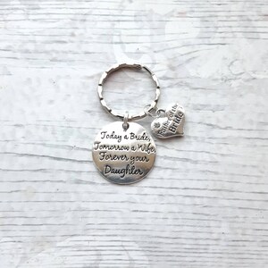 May include: Silver keychain with a round charm that reads "Today a Bride, Tomorrow a Wife, Forever your Daughter". A smaller heart charm with the text "Father of the Bride" is attached to the keychain.