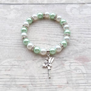 May include: A green and white beaded bracelet with a silver fairy charm. The bracelet is made with faux pearls and rhinestones.