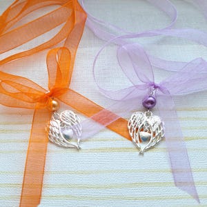 May include: Two angel wing heart charms with a pearl bead on a ribbon. One ribbon is orange and the other is lavender.