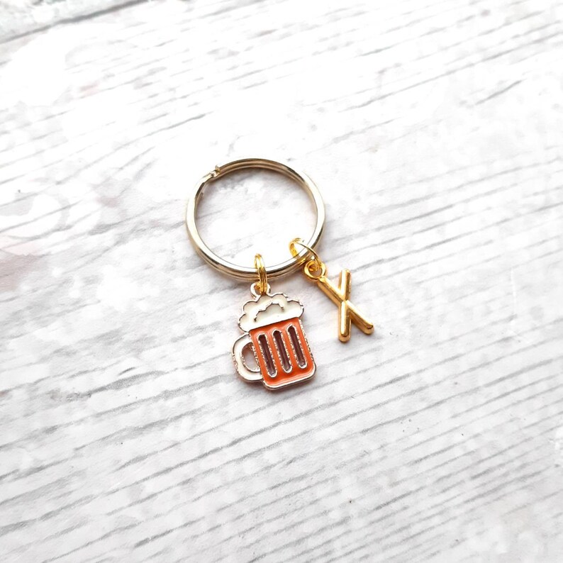 May include: Gold keychain with a beer mug charm and a letter X charm. The beer mug is orange and white.