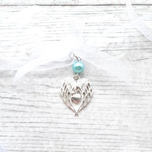 May include: A silver charm with angel wings and a heart pendant, attached to a white ribbon with a light blue pearl bead.