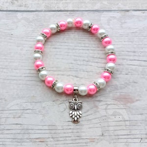 May include: A pink and white beaded bracelet with a silver owl charm. The beads are alternating pink and white with rhinestones.