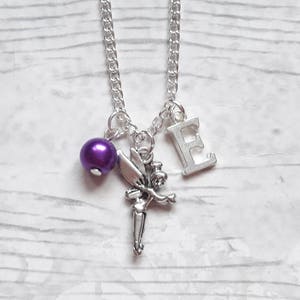 May include: Silver-toned necklace featuring a charm of a fairy, a purple bead, and the letter "E". The chain is a classic link style. The fairy charm is detailed with outstretched arms and wings.