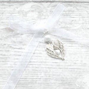 May include: White satin ribbon with a silver angel wing charm with a heart in the center. The charm is attached to a white pearl bead.